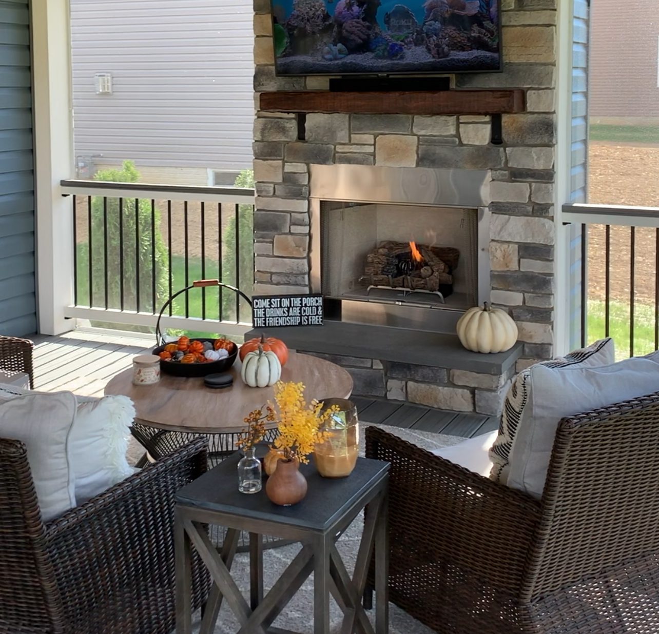 Cozy outdoor deck setup with a fireplace, autumn decorations, and wicker chairs.