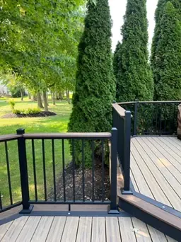 Black railing deck overlooking backyard with green lawn by DreamDecks