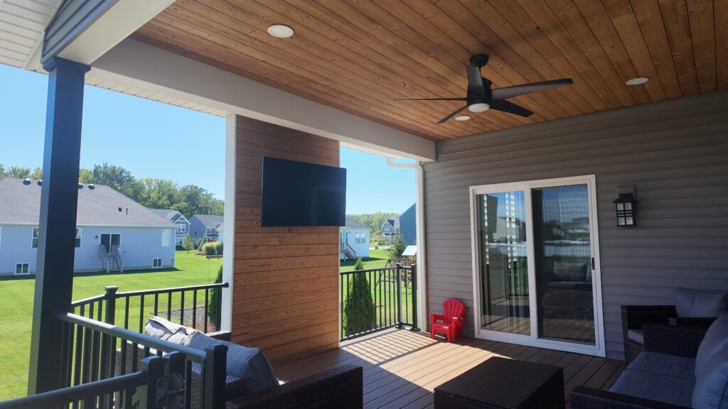 Covered deck in Avon Ohio with a wood ceiling, black ceiling fan, recessed lights, TV accent wall and black aluminum post